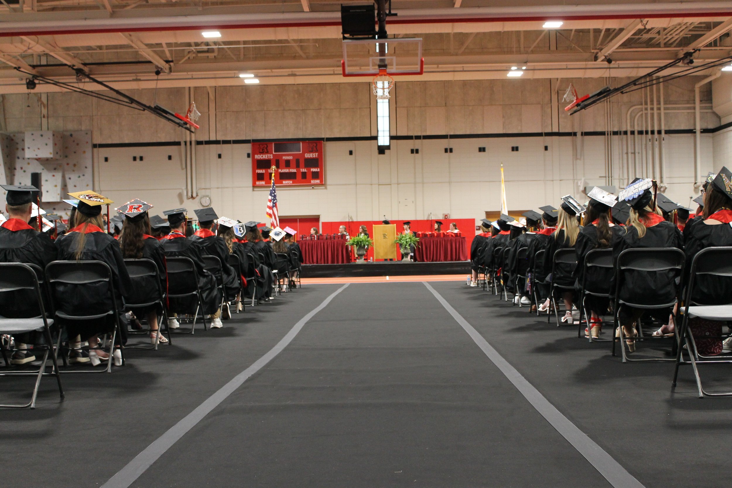 A wide view down the center aisle of the Fieldhouse shows the Class of 2026 seated in rows on either side, with the stage and podium in the distance.
