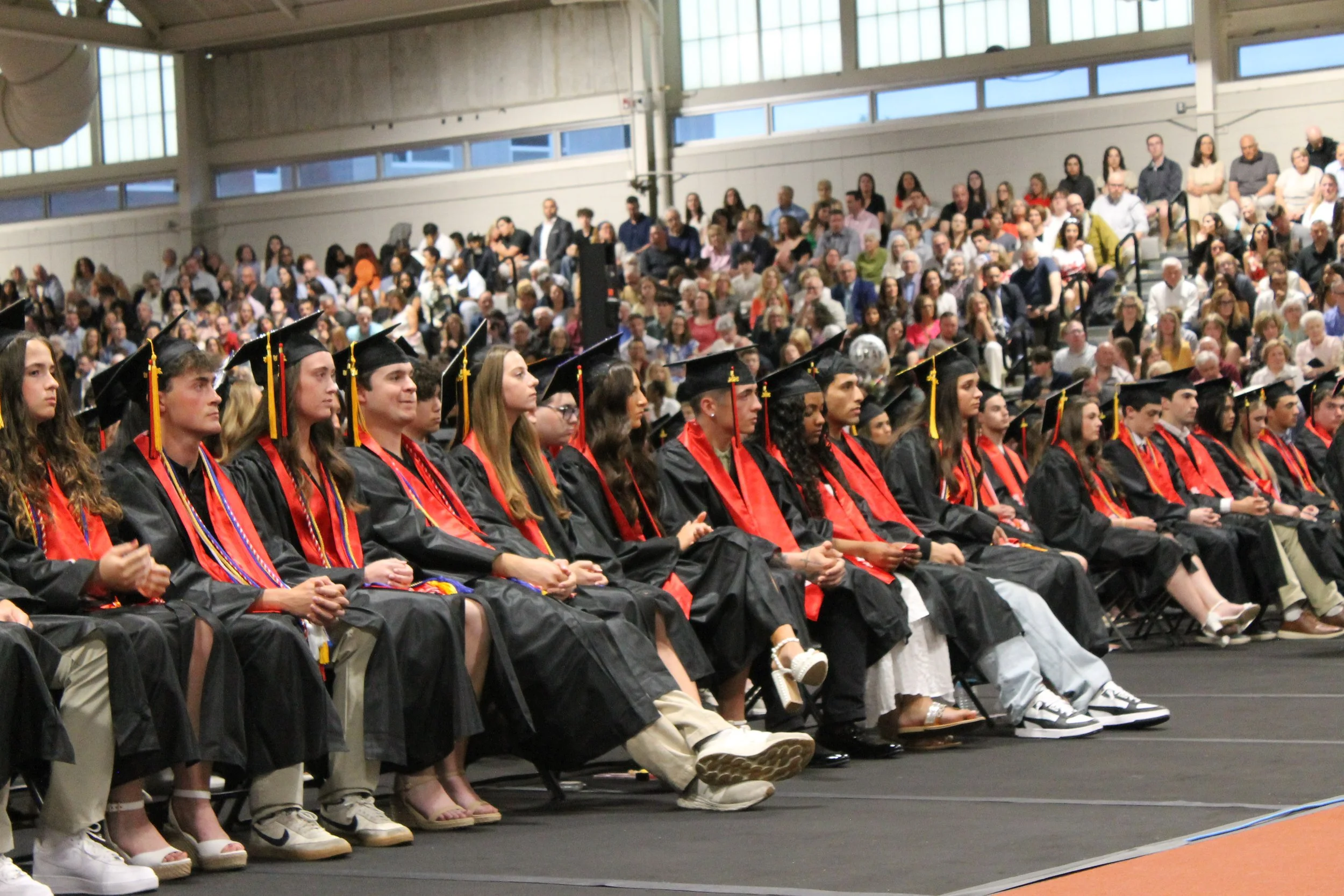 Members of the Class of 2026 sit attentively in their seats as the ceremony gets underway, with a full house visible in the stands behind them.