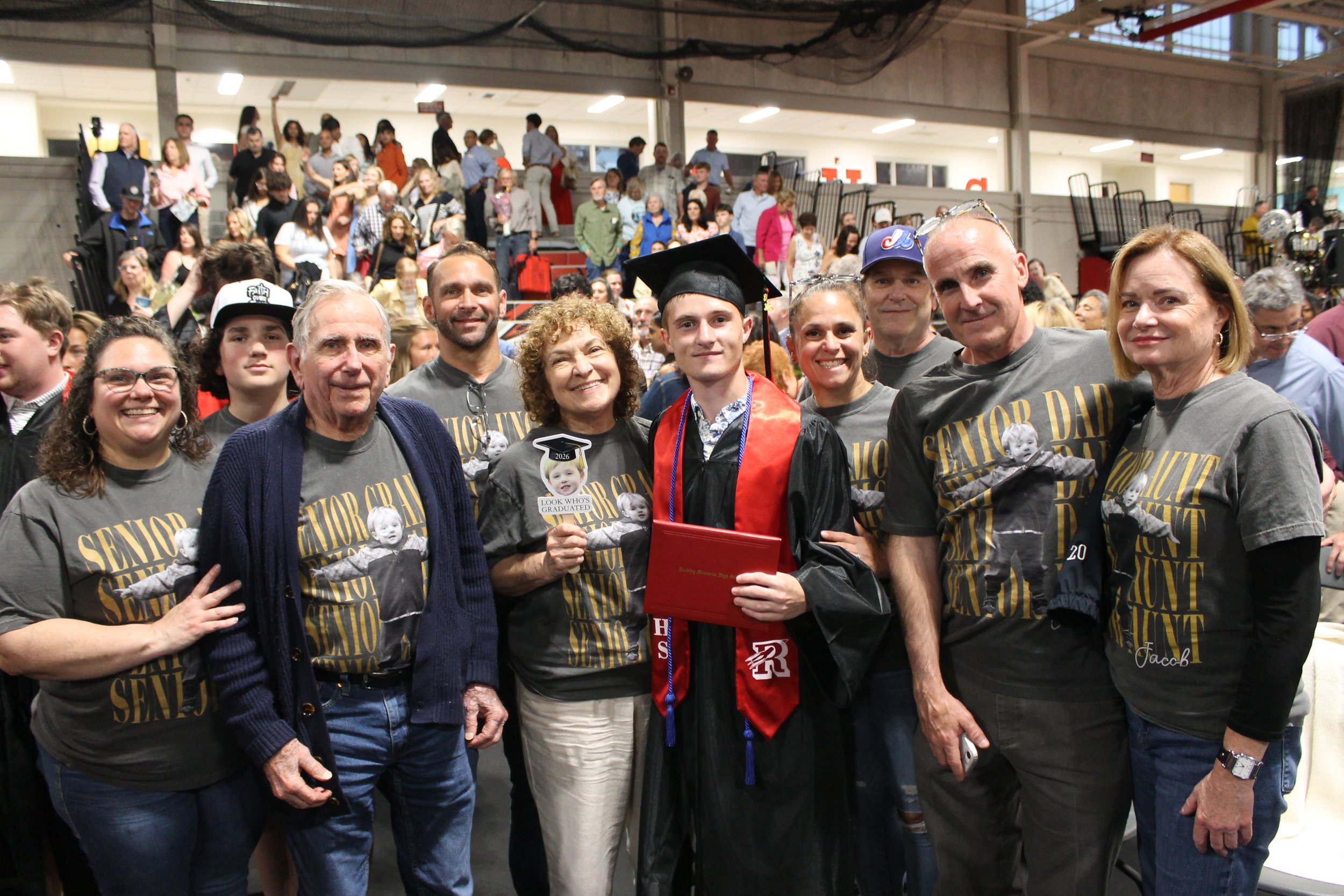 Graduate John Ward pauses for a photo with family members following the ceremony, his family wearing matching shirts in support.