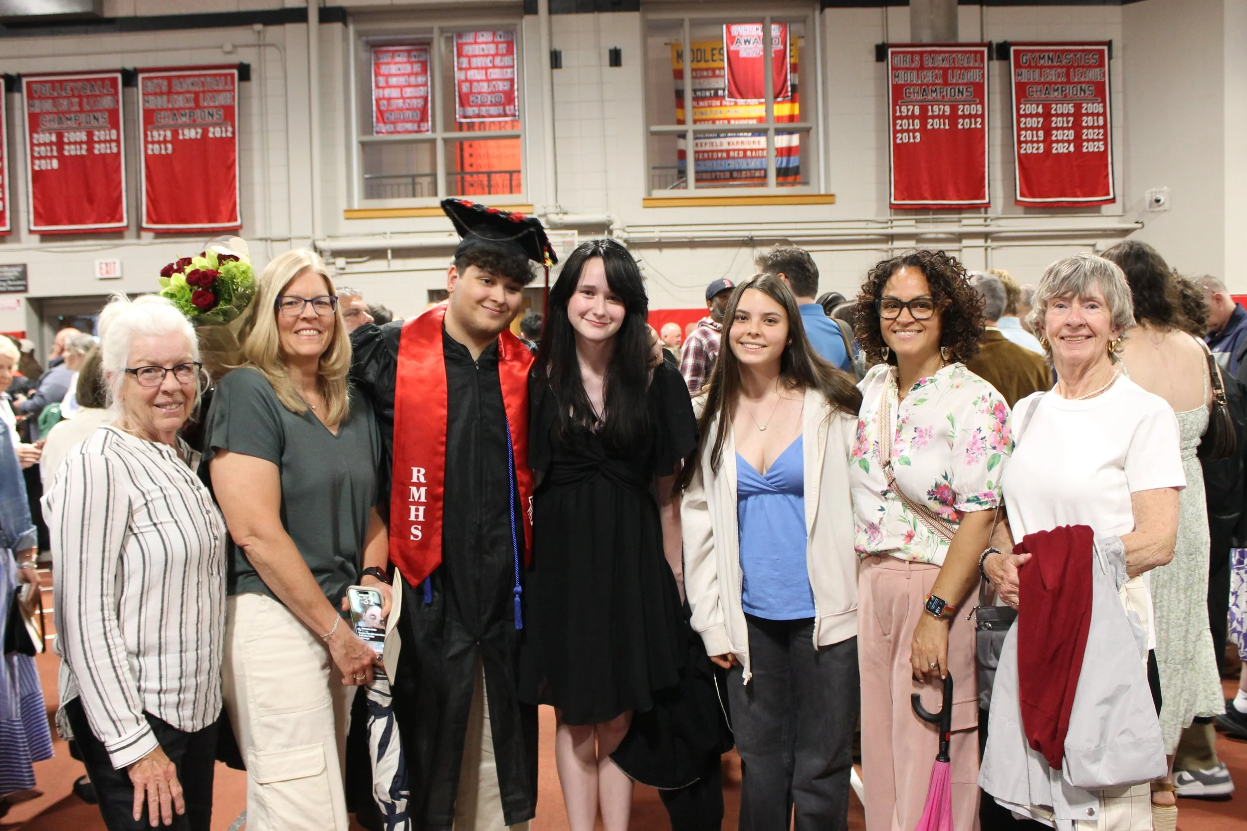 Graduate Carson Beaulieu pauses for a photo with family members following the ceremony, beneath the champsionship banners lining the walls of the Fieldhouse.