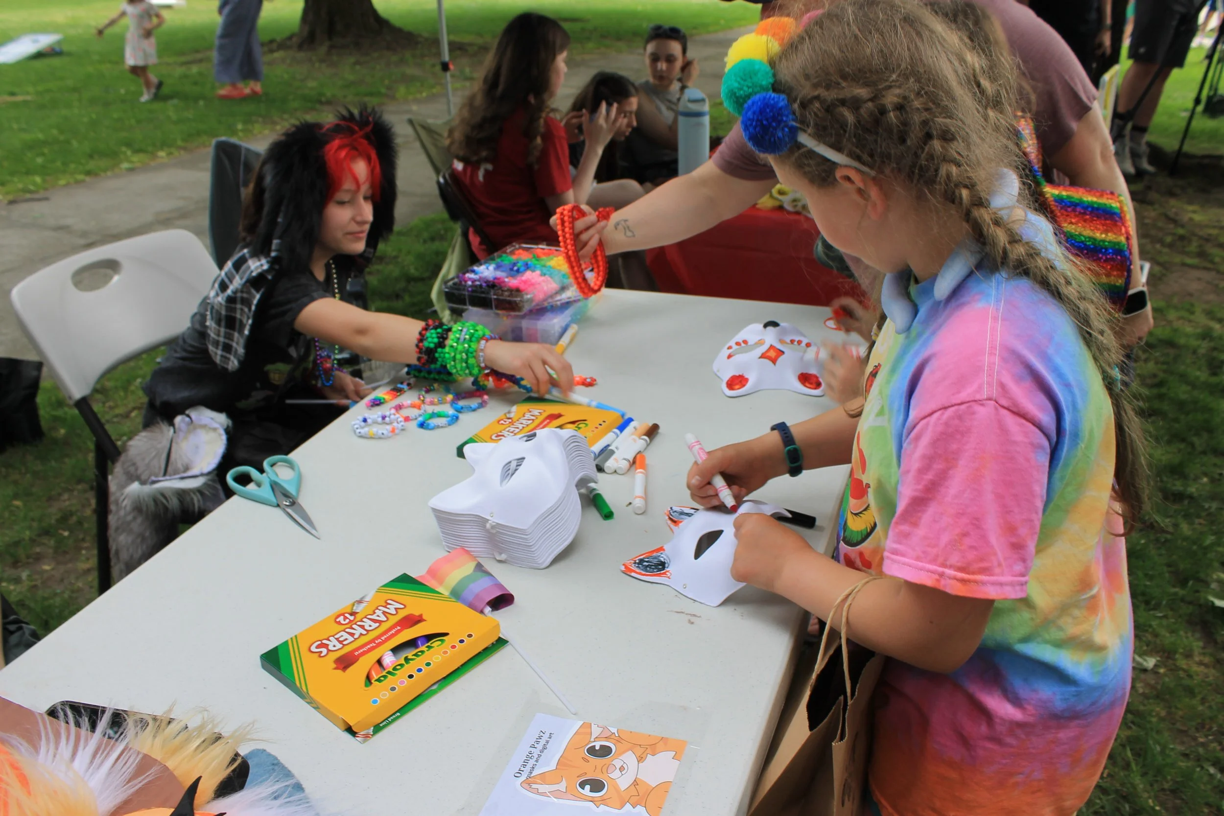 Young attendees decorate masks and make bead jewelry at a crafts table on the Common during the pride celebration.