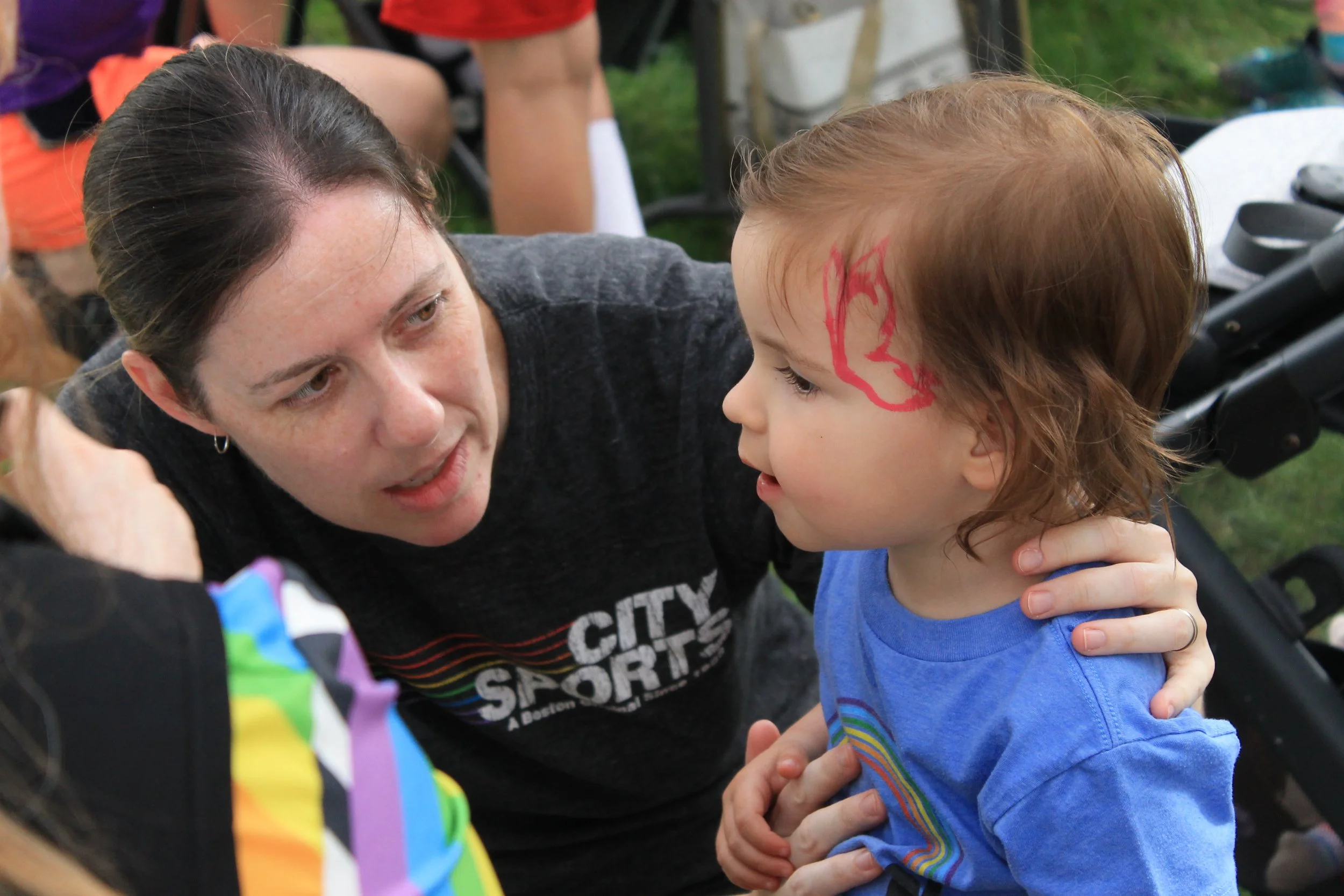 A parent and young child, sporting fresh face paint, share a moment on the Common during the Pride celebration.