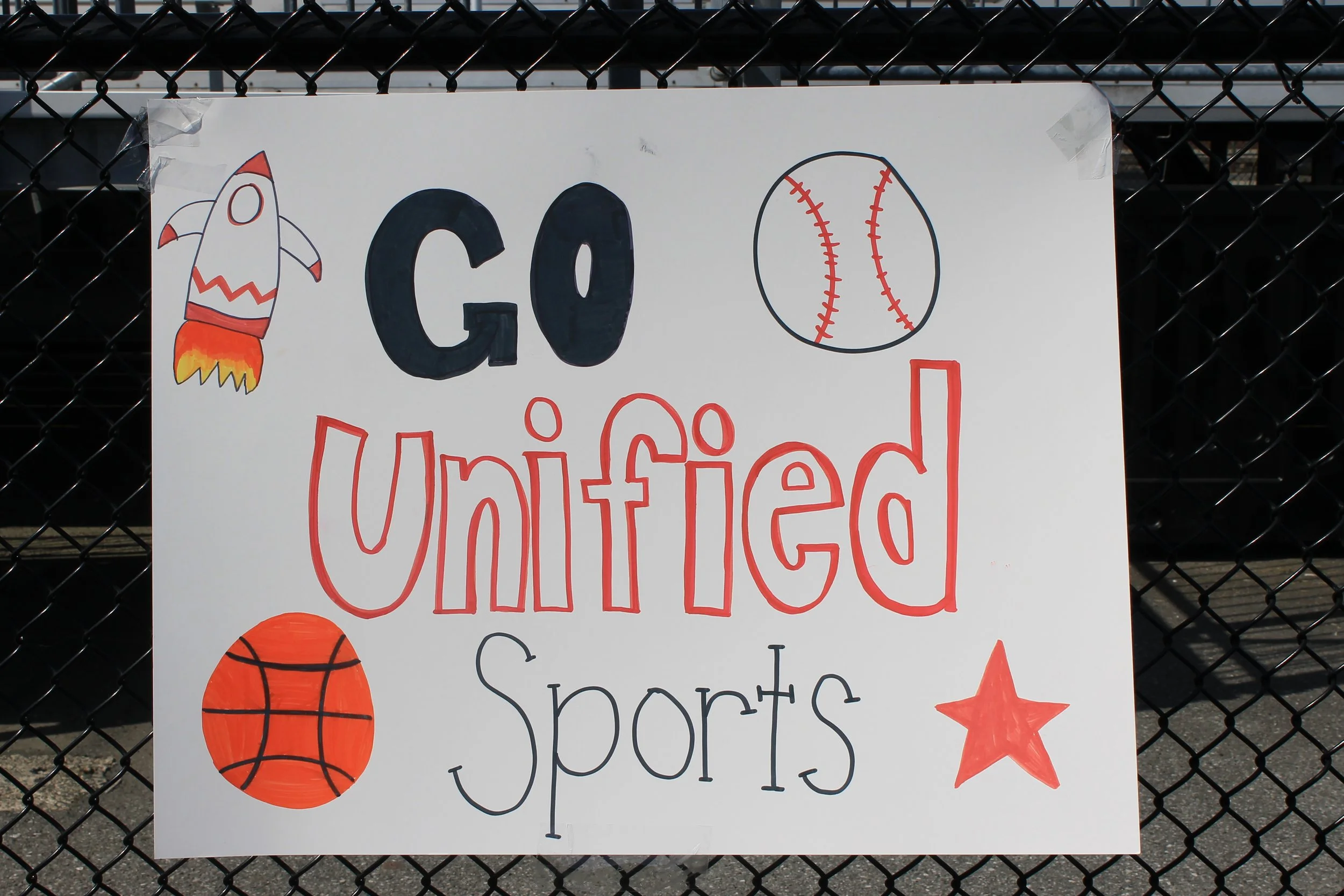 A hand-made "Go Unified Sports" sign decorates the fence, cheering on all the Unified athletes.