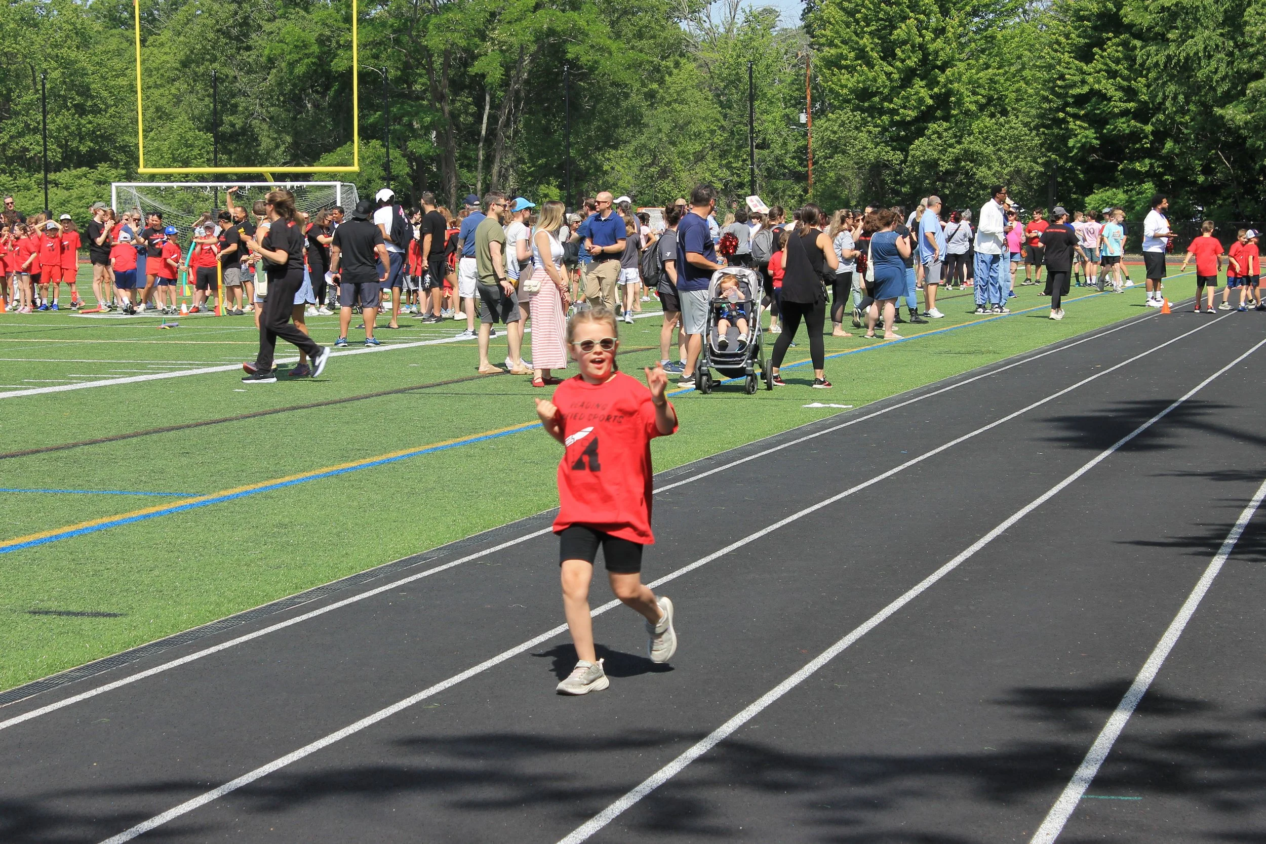 A young athlete in a Reading Unified Sports shirt smiles and waves while sprinting down the track.