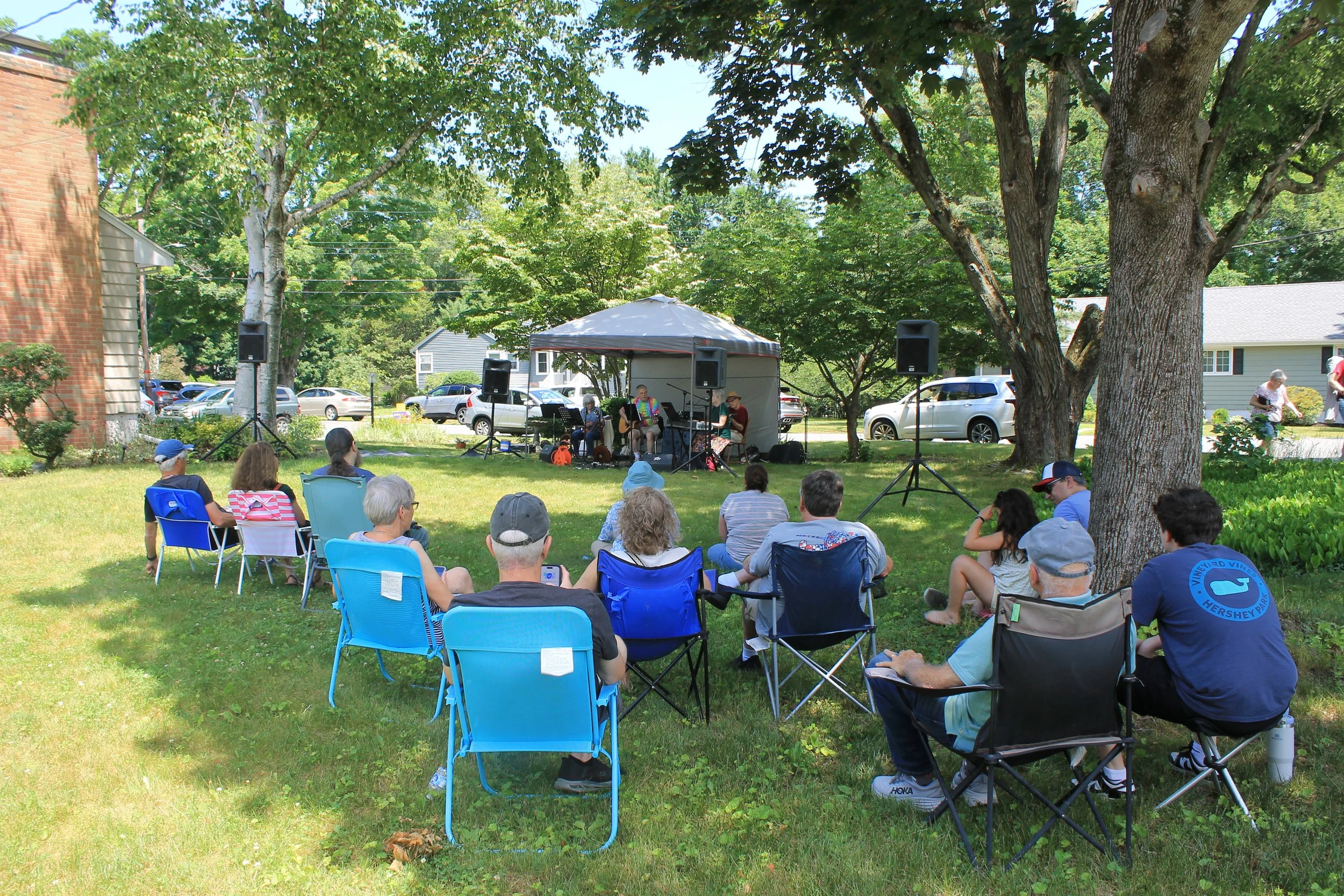People gather at 24 Linnea Lane on lawn chairs, watching  The Neighbors perform under a tent.