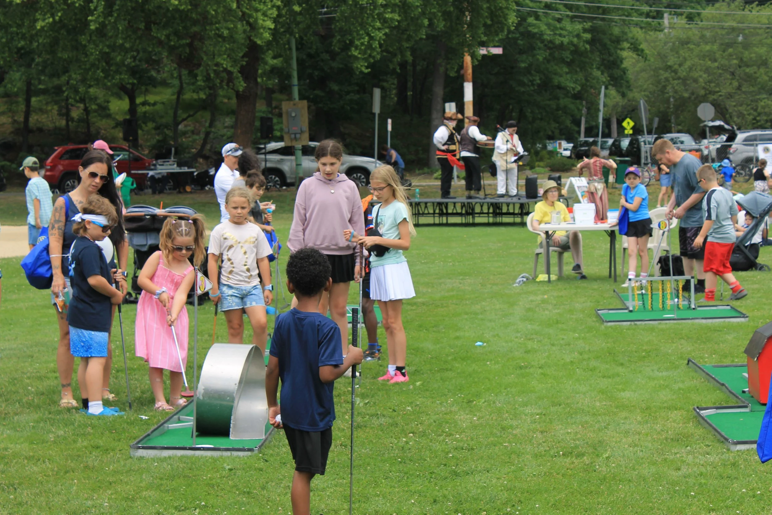 Kids work their way through the mini golf course while a band plays on the stage behind them.