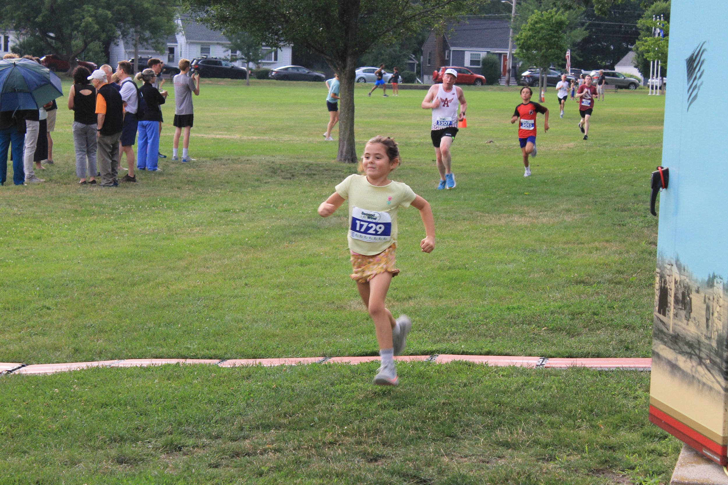 A young runner sprints across the finish line at Memorial Park as more participants close in behind.