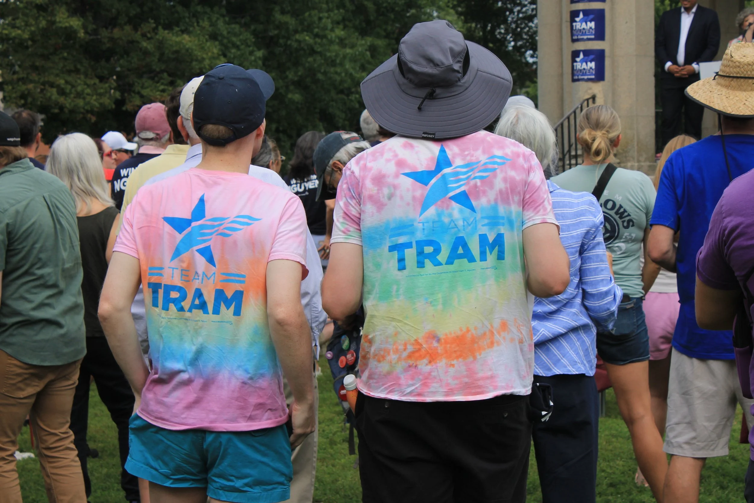Two rally attendees from behind, wearing tie-dye "Team Tram" t-shirts with a blue star logo.