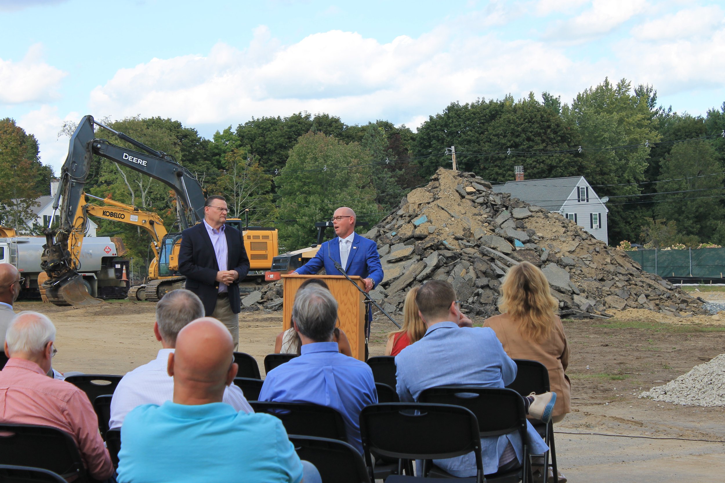 State Rep. Brad Jones (left) and Rep. Rich Haggerty (right) address the crowd at the Killam School groundbreaking, with construction equipment in the background.