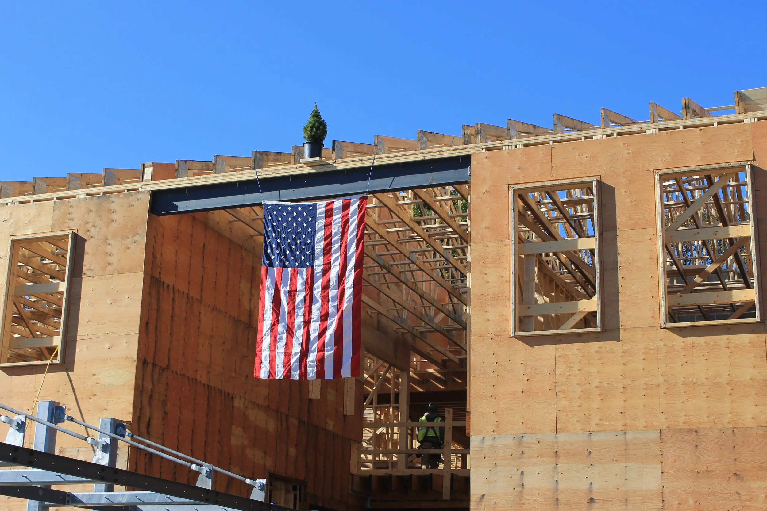 A U.S. flag and a small evergreen tree mark the final beam at the new ReCAL facility.
