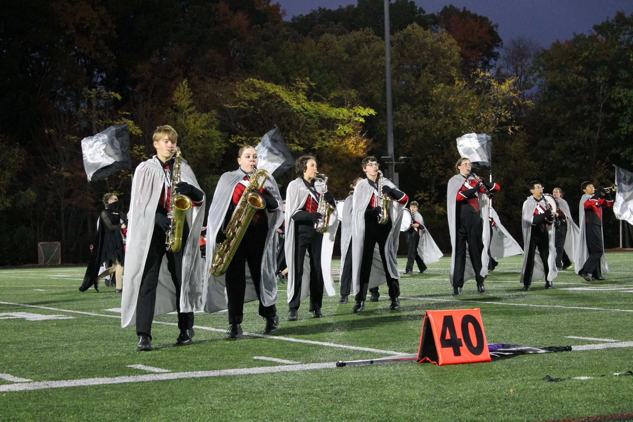 Saxophone, woodwind players, and color guard advance toward midfield during RMHS's Home Show performance.
