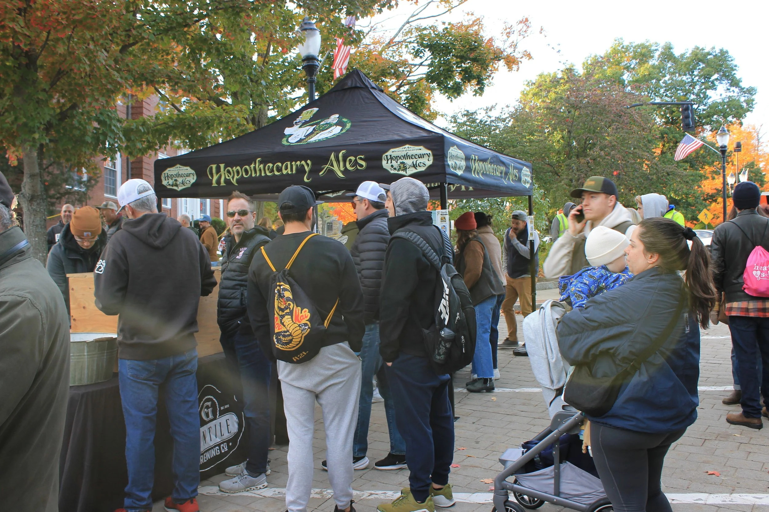 Attendees gather on the cobblestone in front of the Hopothecary Ales tent.