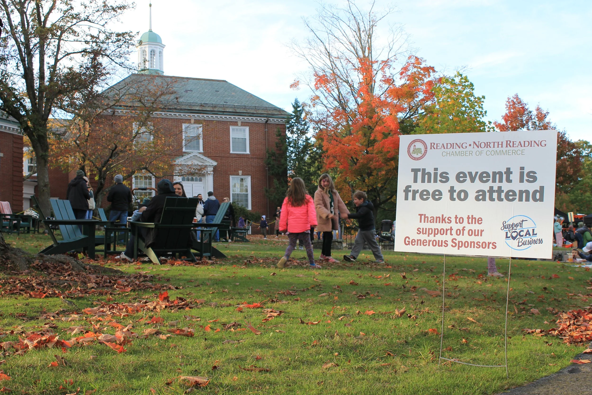 Children play on the Town Common beside a sign noting the Chamber's event is free to attend.