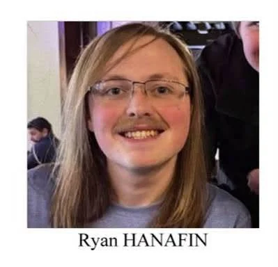 Photo of Ryan Hanafin, a white man with long reddish-brown hair, glasses, and a mustache, wearing a gray shirt.