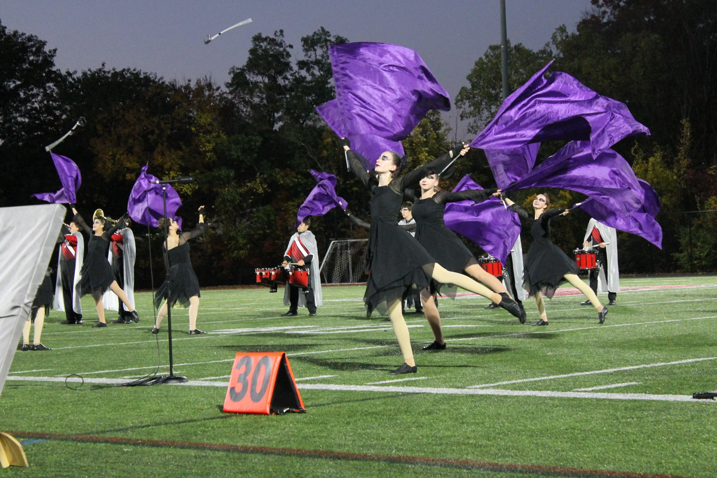 RMHS color guard members in black costumes leap while waving purple flags during the band’s “Nevermore” halftime show.
