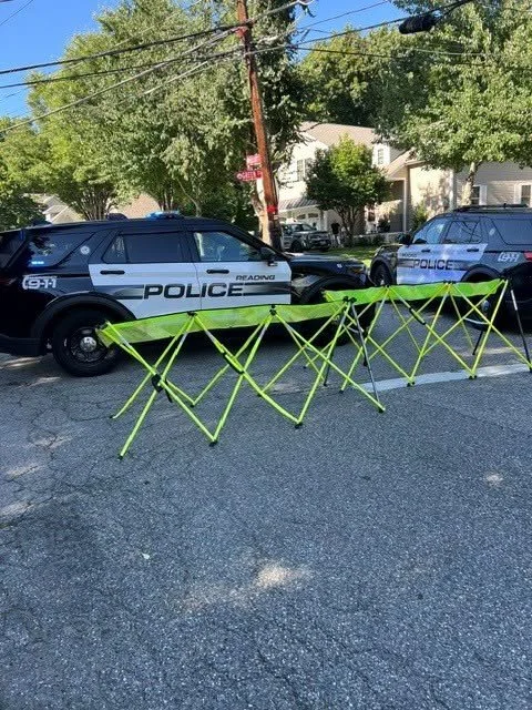 Two Reading police SUVs and a bright green folding barrier blocking a residential street on a sunny day.