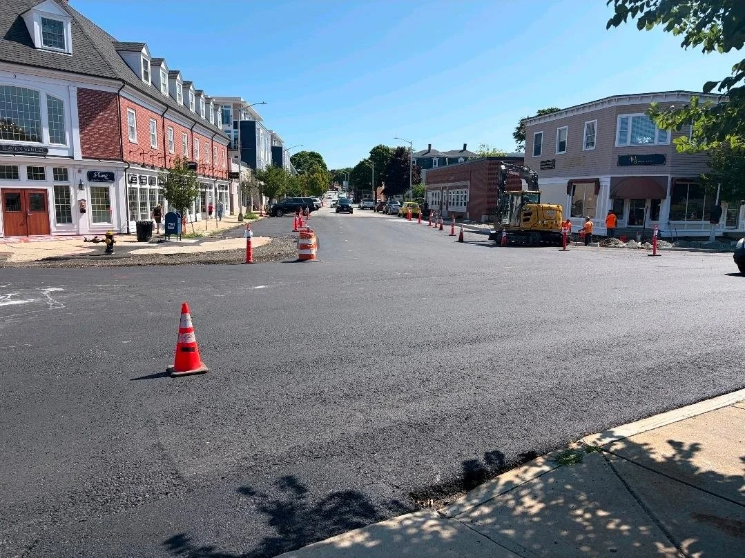 Newly paved downtown Reading street lined with orange cones, with a construction crew and excavator working near storefronts on Haven Street.