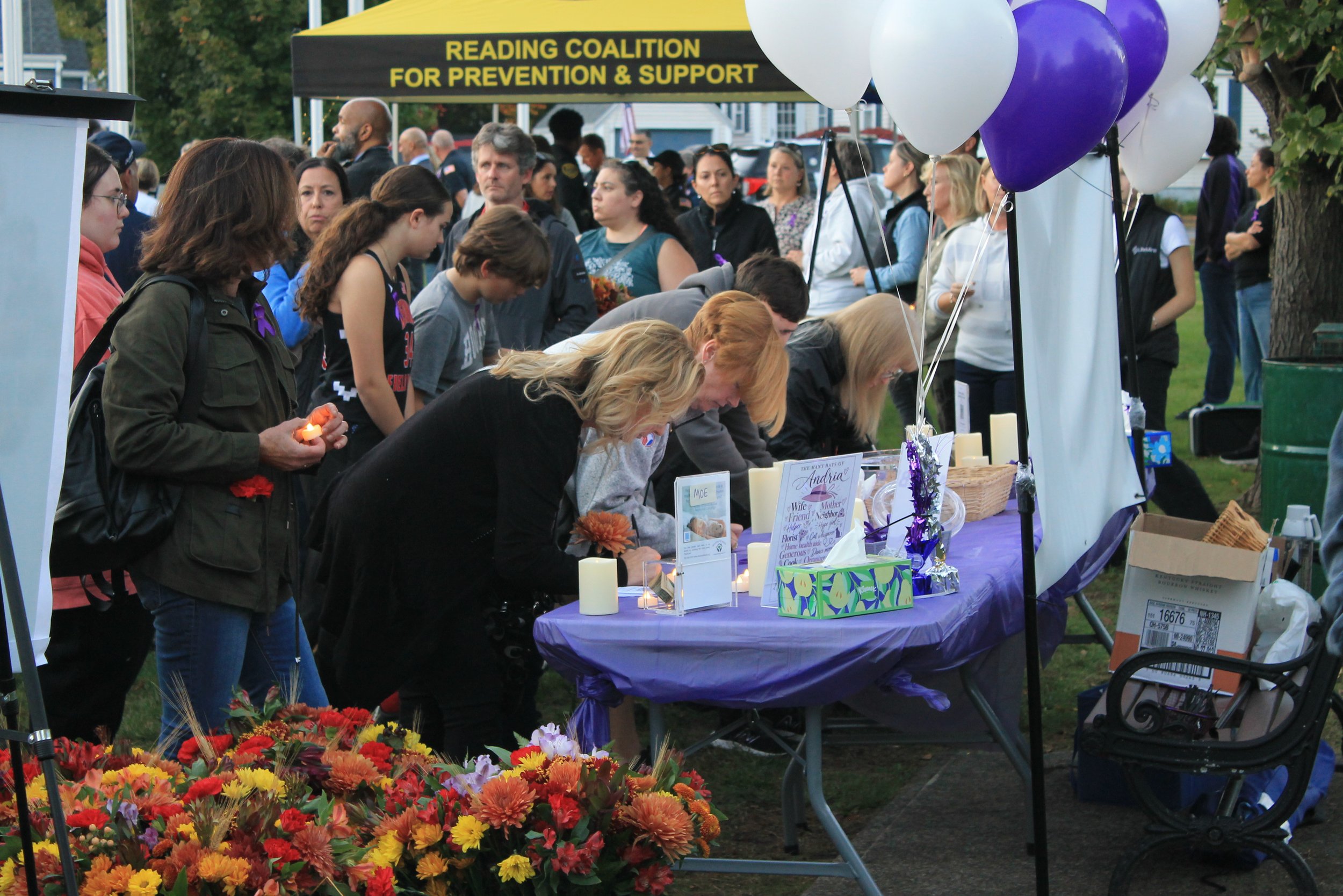 Memorial table with a banner for Andria Hanafin, , candles, flowers, and purple and white balloons, where attendees wrote messages for Andria’s family.
