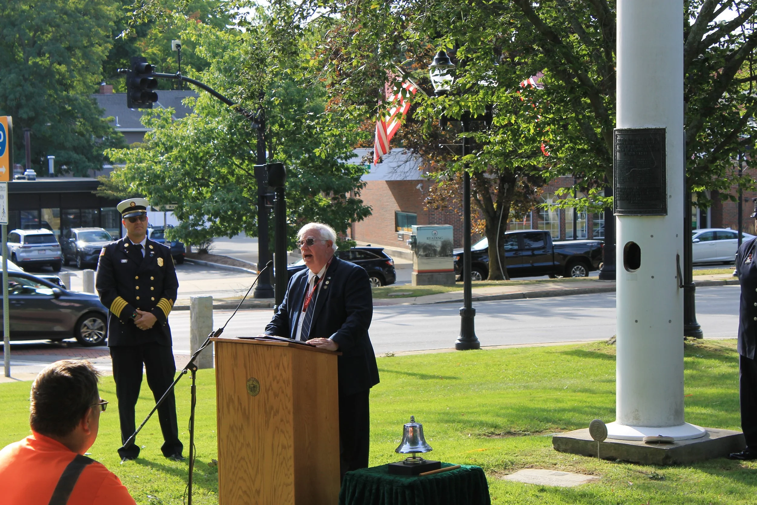 An older man in a suit speaks at a podium as the fire chief stands behind him during the ceremony.