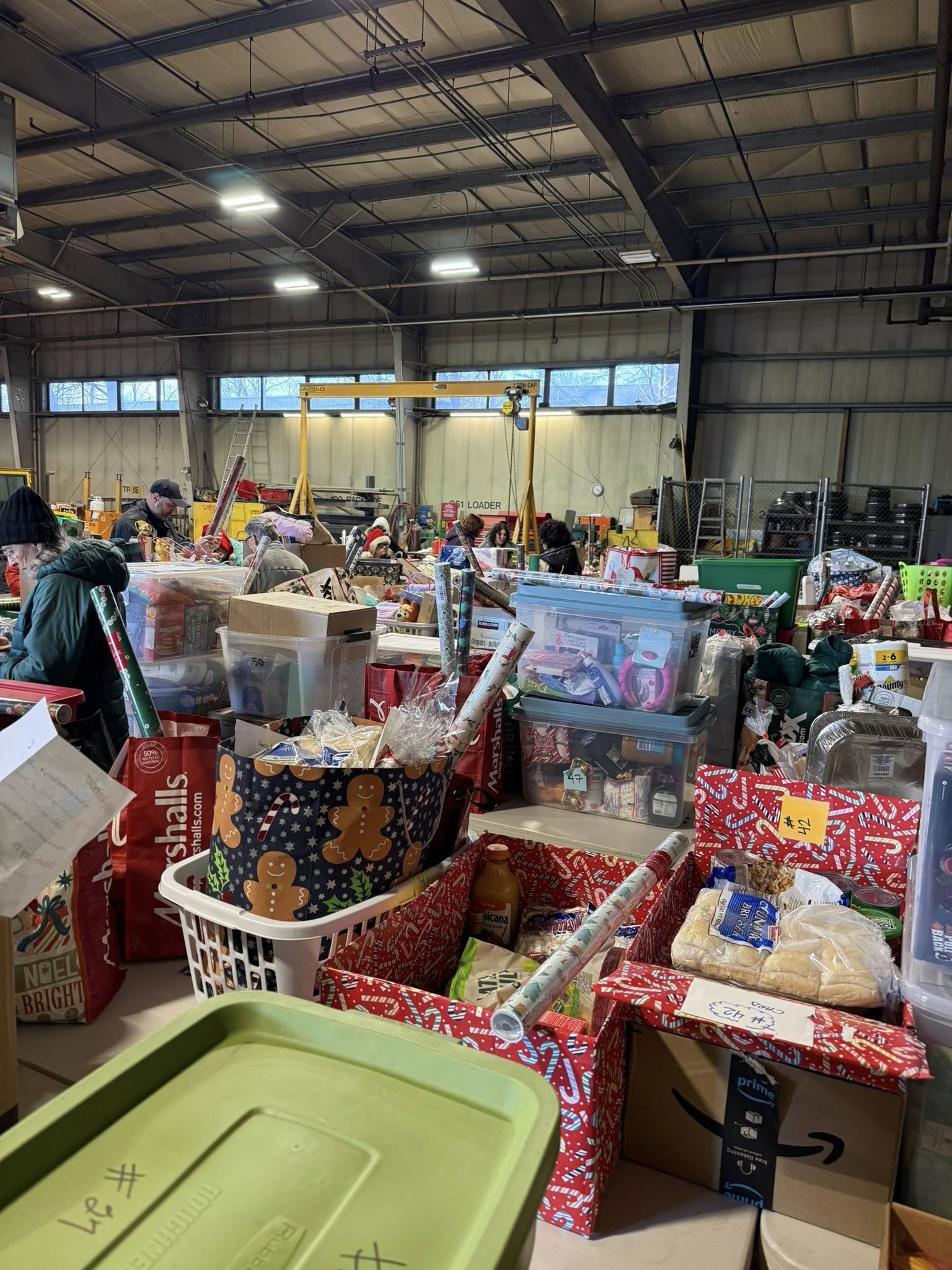 Volunteers sort and organize bins of wrapped gifts, food, and holiday supplies in a warehouse for the Reading Adopt-A-Family Program.