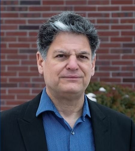 Man with grey and white hair with a brick background