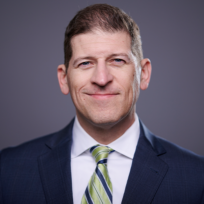 Headshot of David Solet, a middle-aged white man with short hair, wearing a blue suit and a green tie with blue stripes.