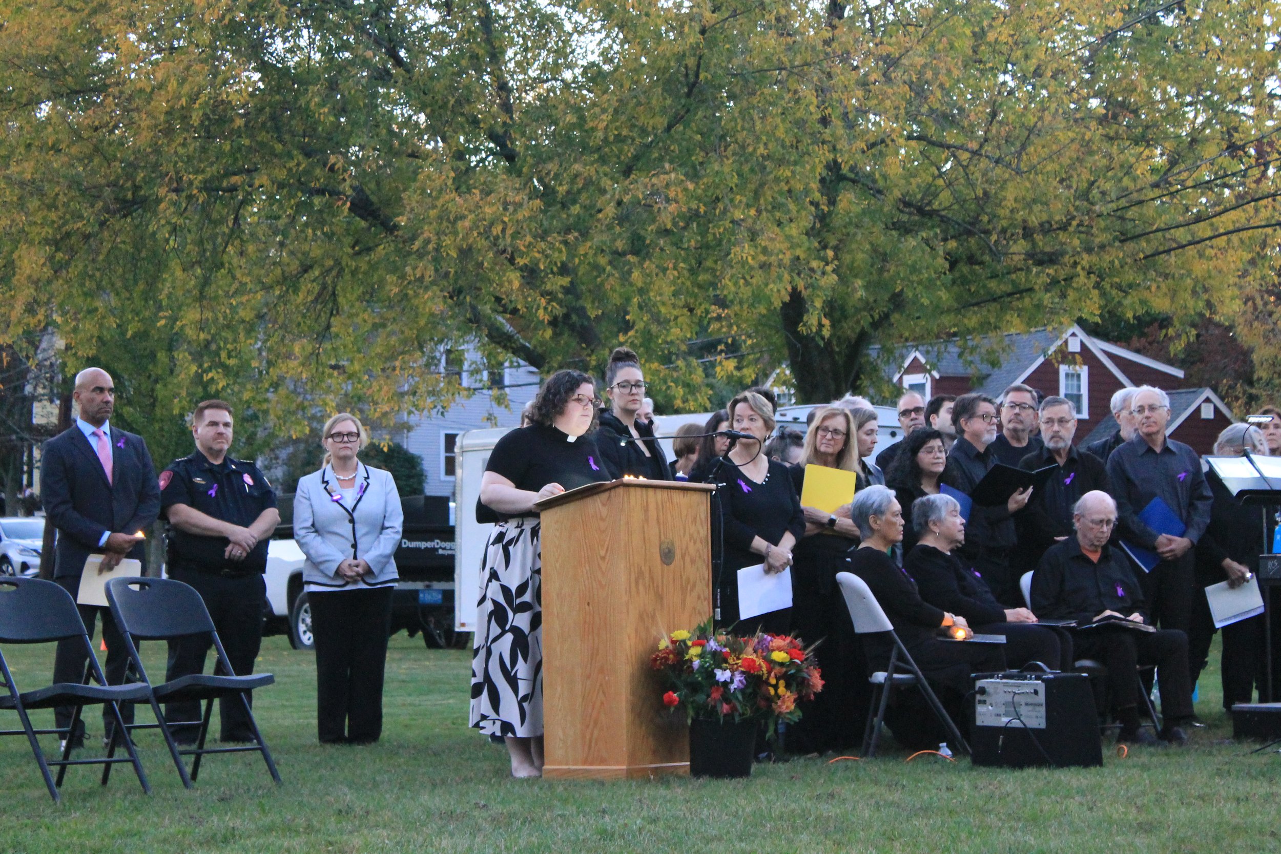 A woman in a clerical collar speaks at a podium as officials and choir members stand nearby at the vigil for Andria Hanafin.