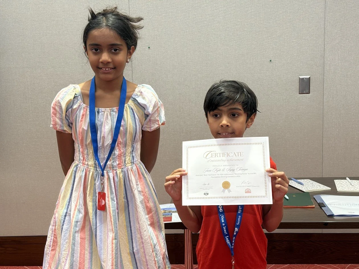 Two children stand together in the library Community Room, one holding a certificate of achievement.