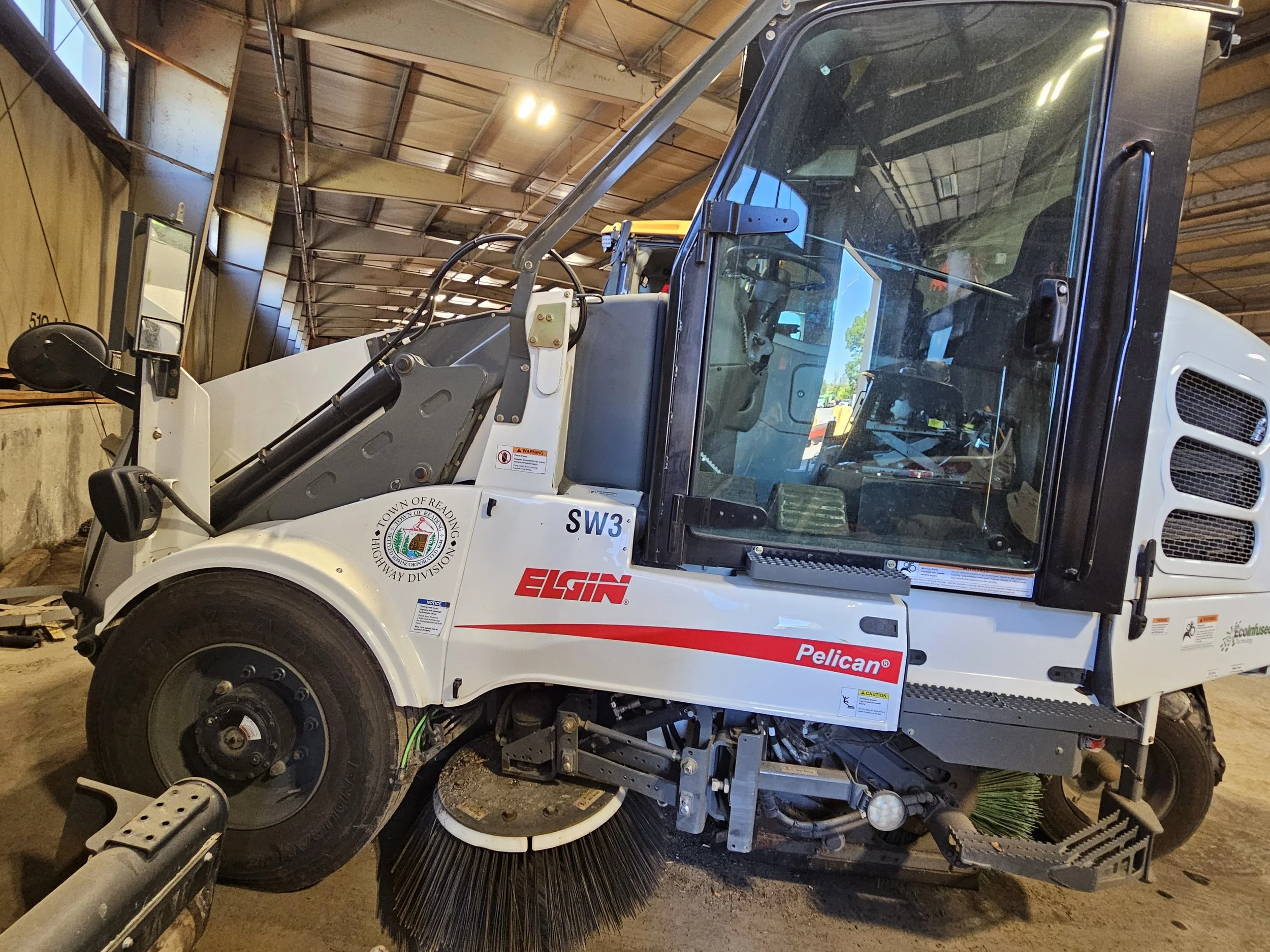 A white Elgin Pelican street sweeper marked “Town of Reading Highway Division” and labeled SW3, parked inside a garage.