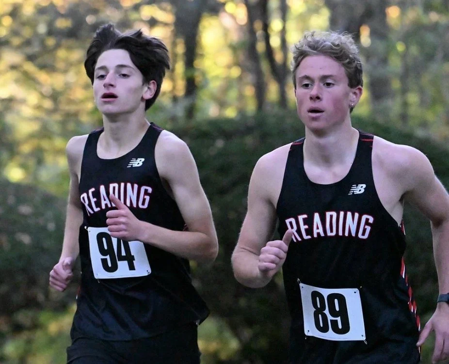 Two Reading boys in black uniforms, bibs 94 and 89, run side by side on a wooded course.