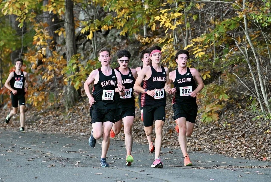 Four Reading boys cross-country runners in black uniforms run together along a wooded trail during a meet.