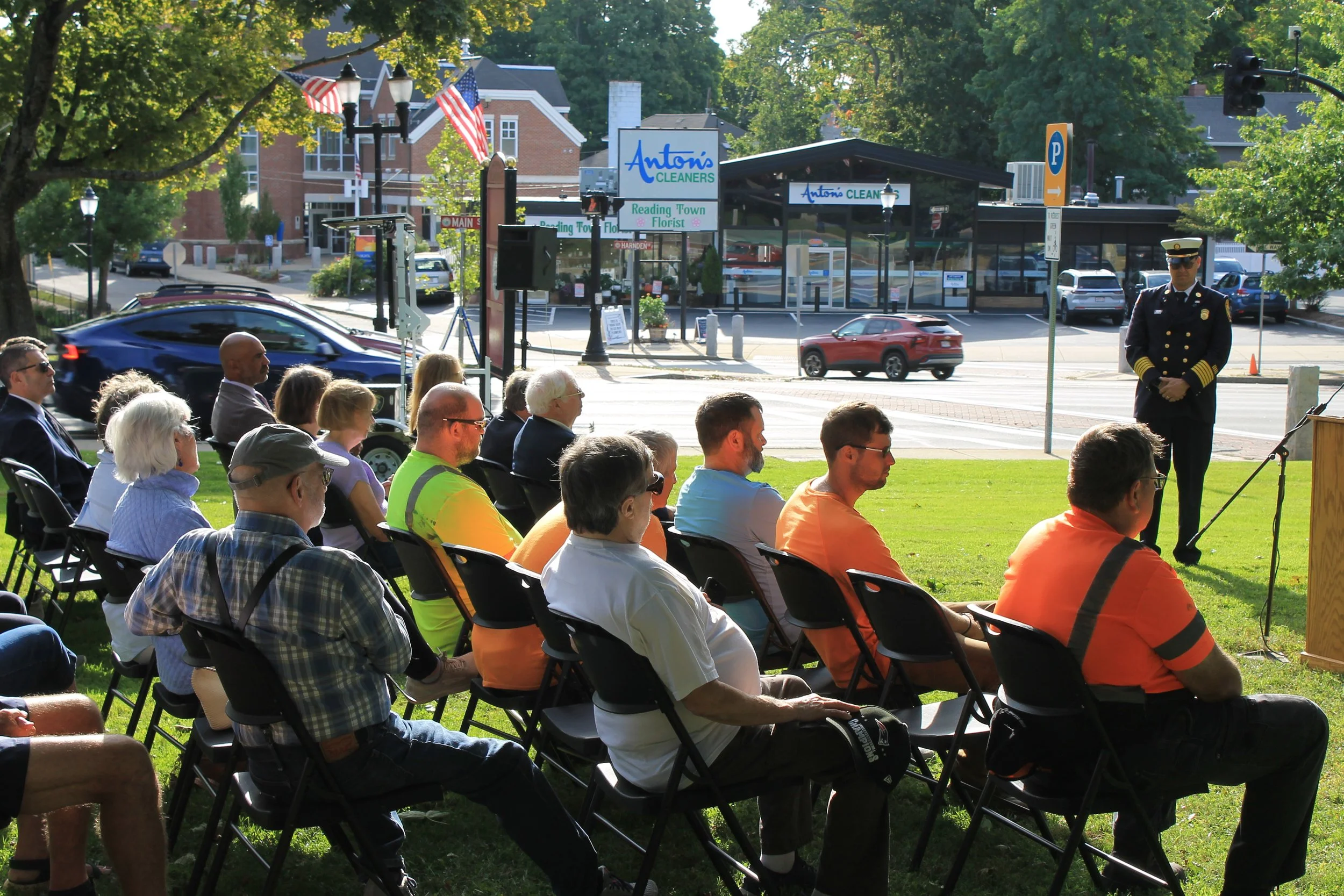 Rows of seated attendees, including Department of Public Works workers in orange shirts, listen during a 9/11 ceremony on the town common.