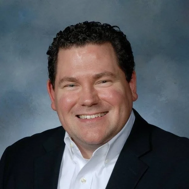 A short brown hair gentleman with a white dress shirt and dark blazer.