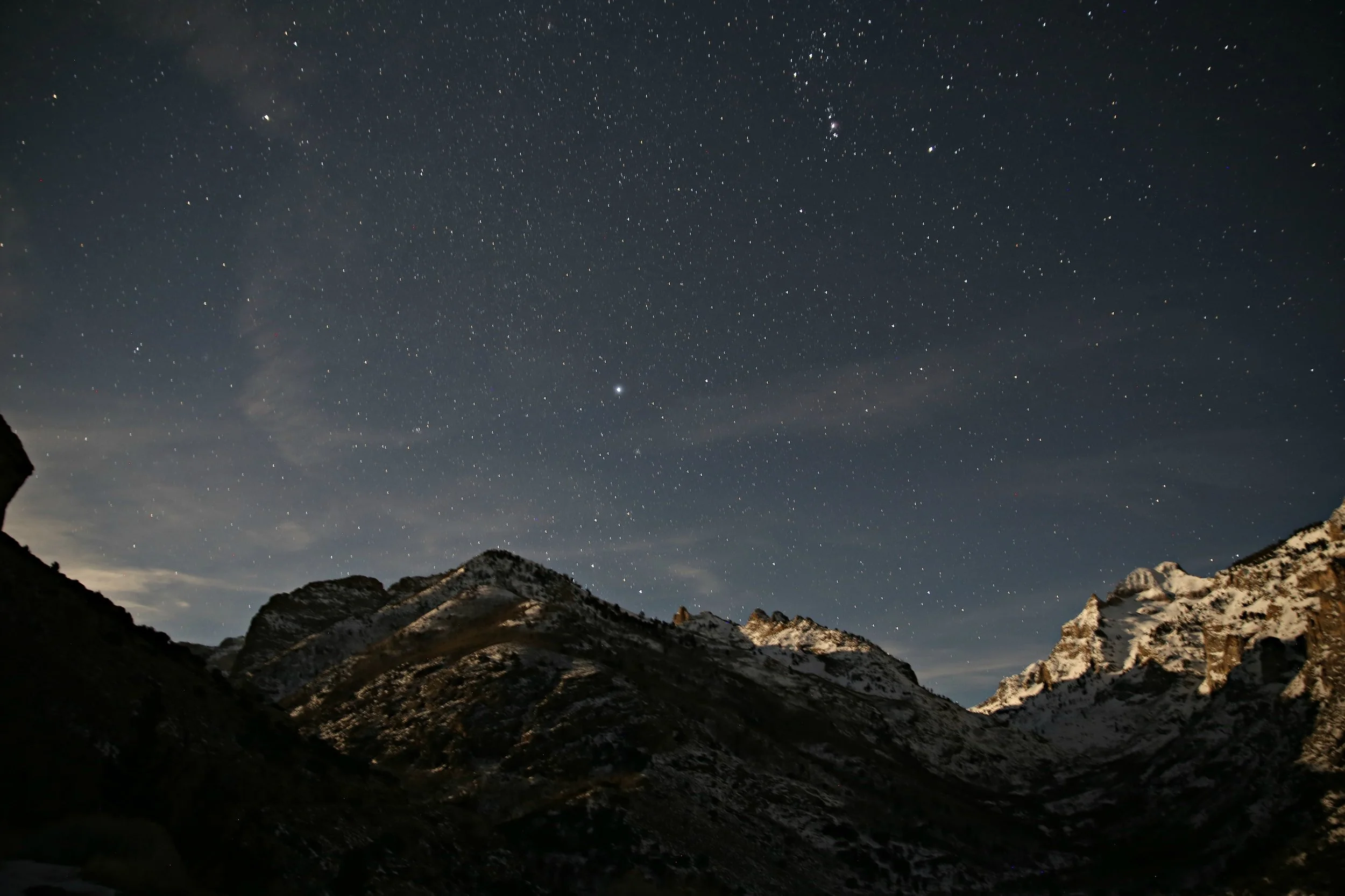 Night sky filled with stars over rugged mountain landscape with snow-capped peaks.