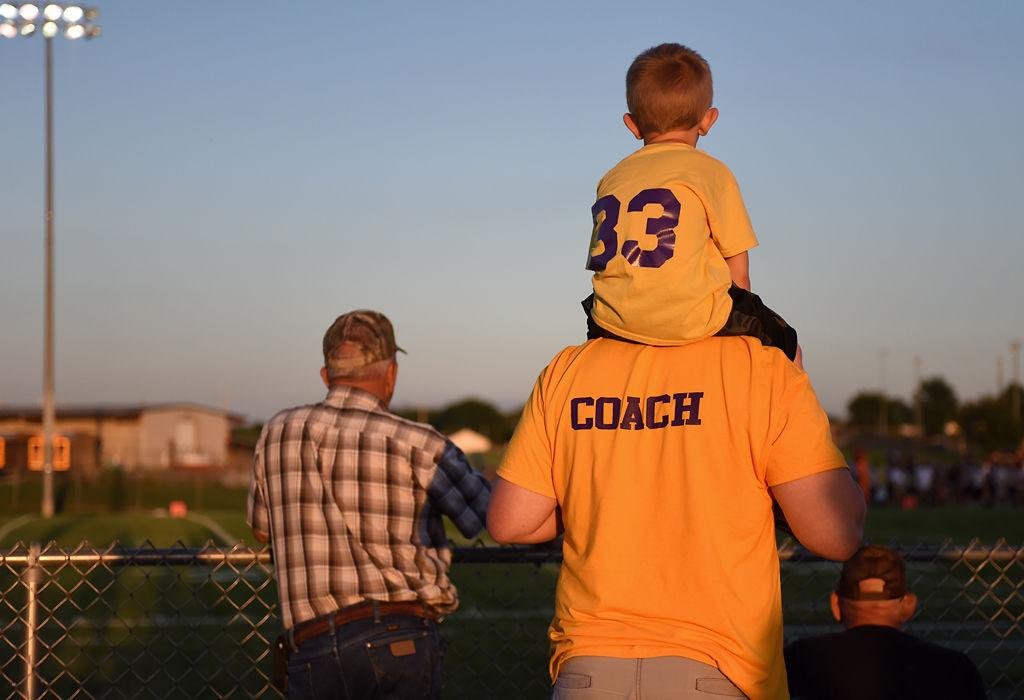 Ray Ensley watches a football game between Hallsville High School and Osage High School seated on the shoulders of his father, Erik Ensley, on Friday at Hallsville.