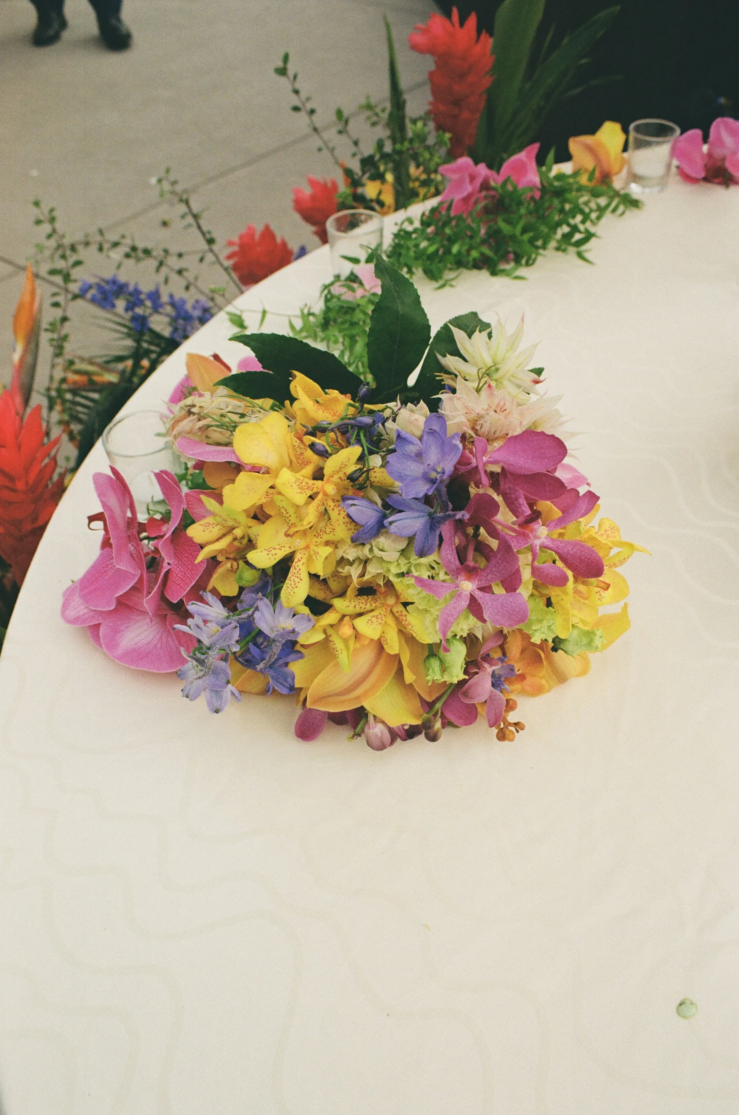 Colorful flower bouquet on a white tablecloth with other floral arrangements in the background.