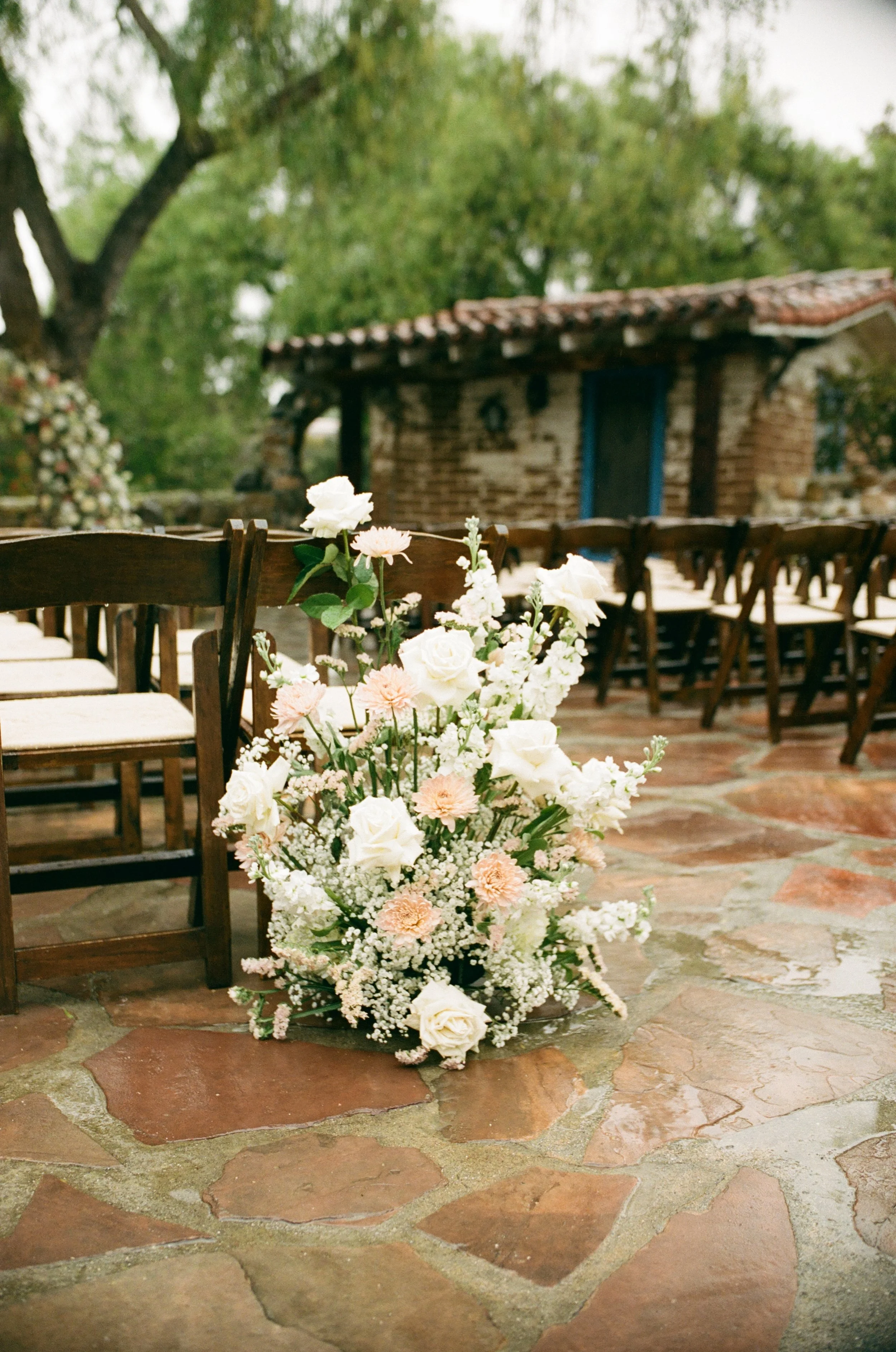 A floral arrangement with white roses and pink carnations on a stone patio at an outdoor event setup.