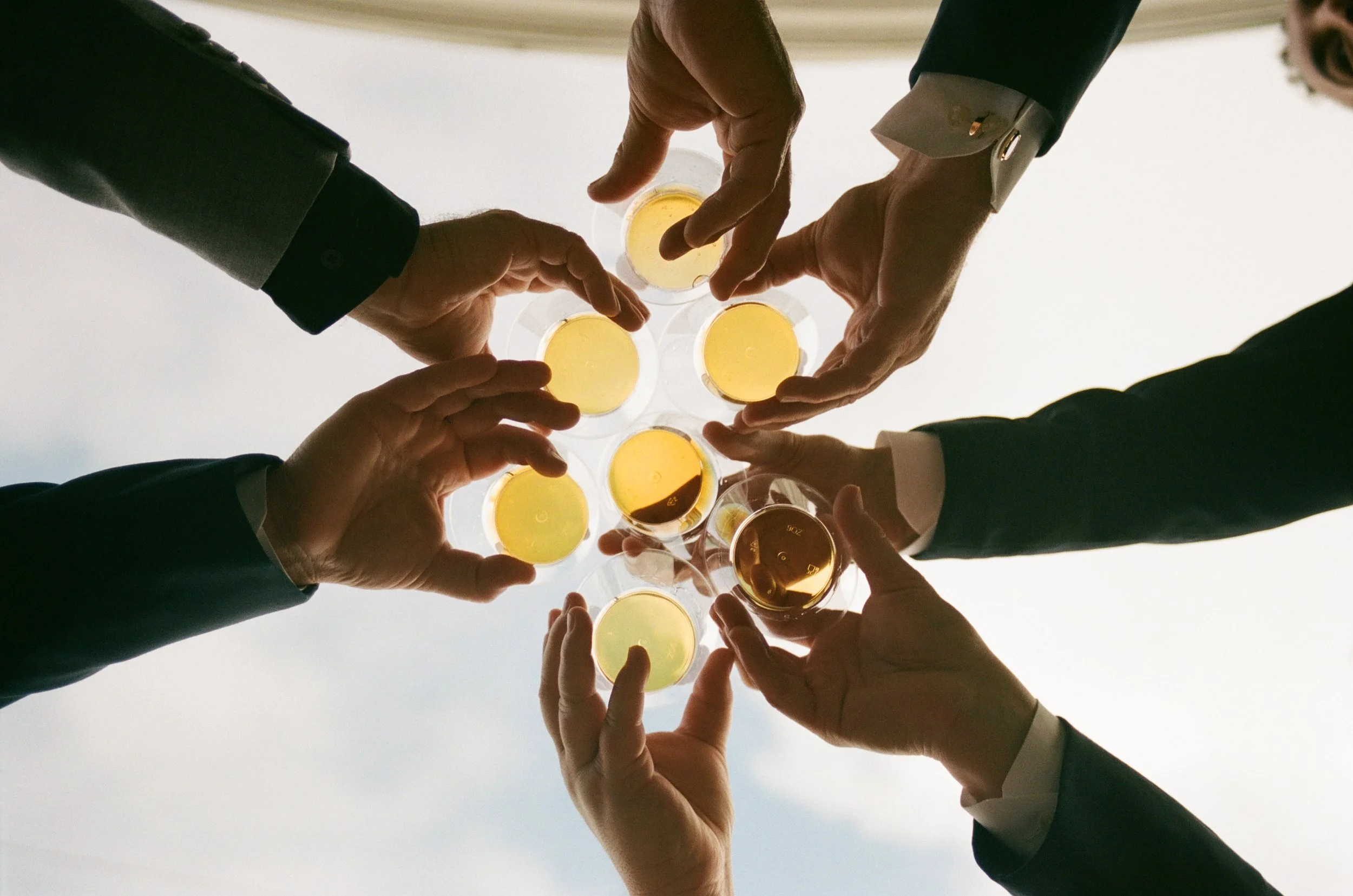 People in business suits raising glasses of champagne in a toast, seen from below against a cloudy sky.