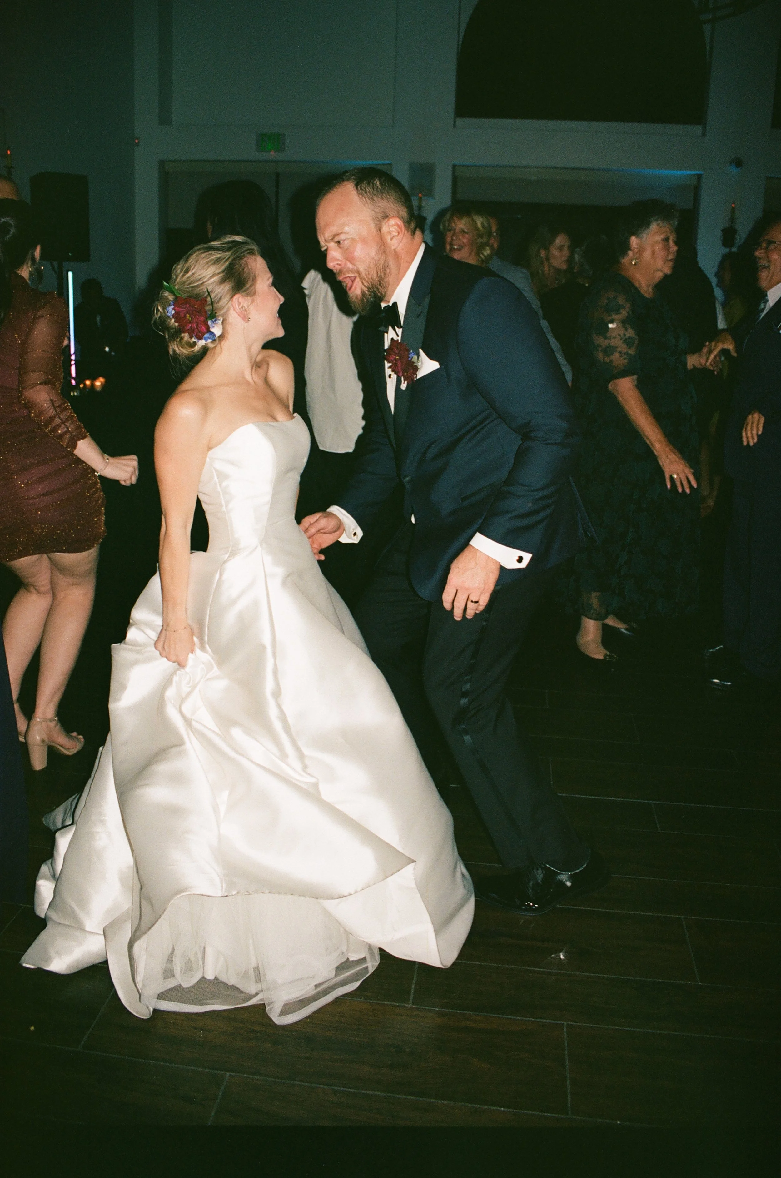 A bride and groom dancing at a wedding reception, with other guests dancing in the background.