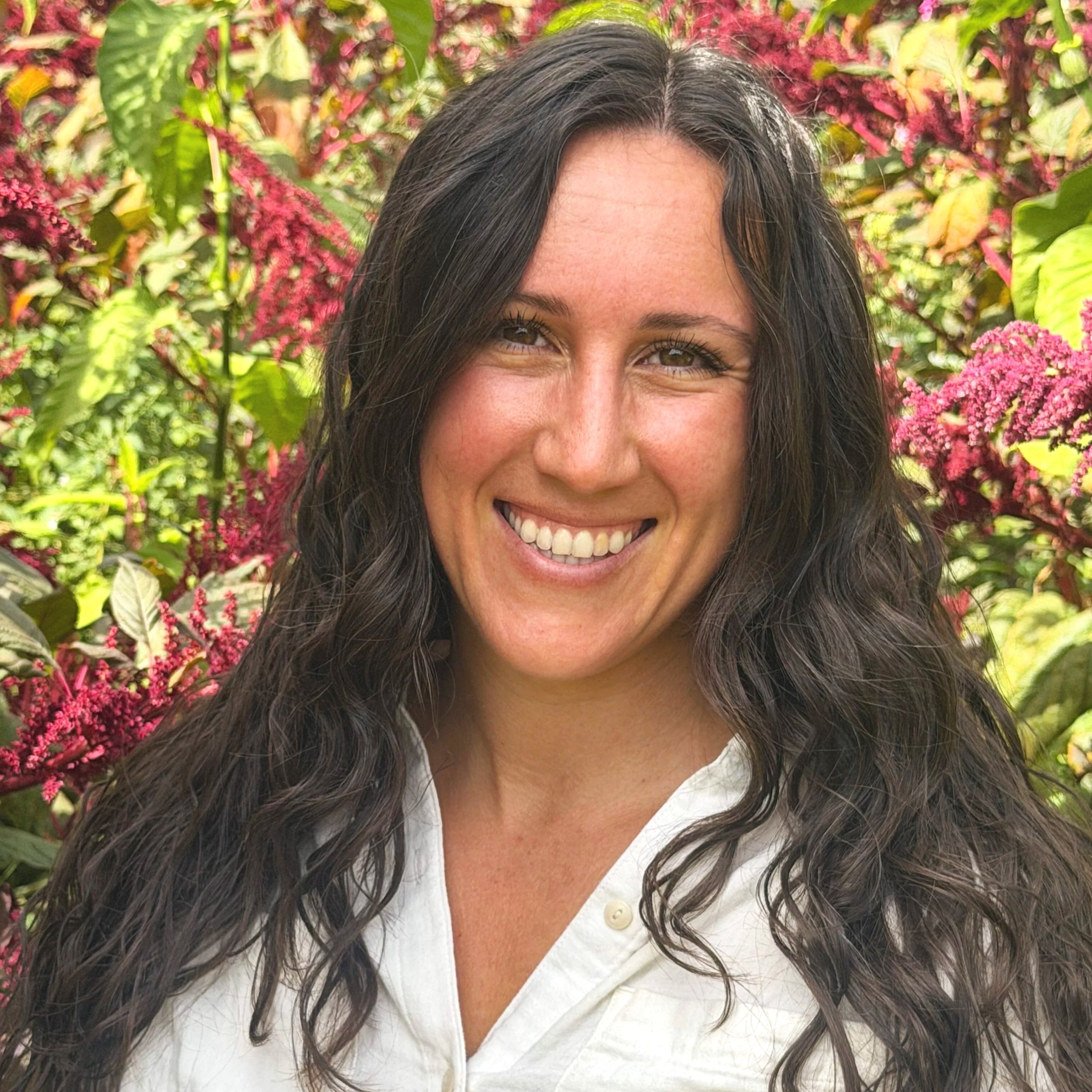 A woman with curly brown hair smiling and hugging a large black and white dog against a black background.