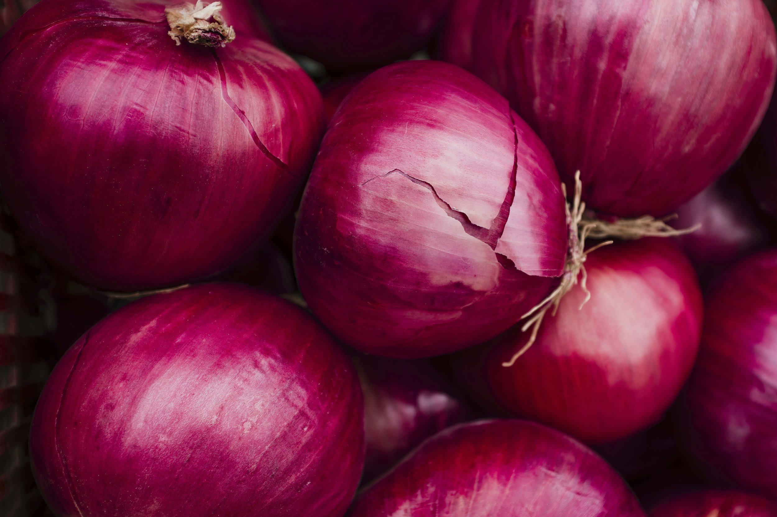 Red onions with purple and white skins, some with cracks, piled together.