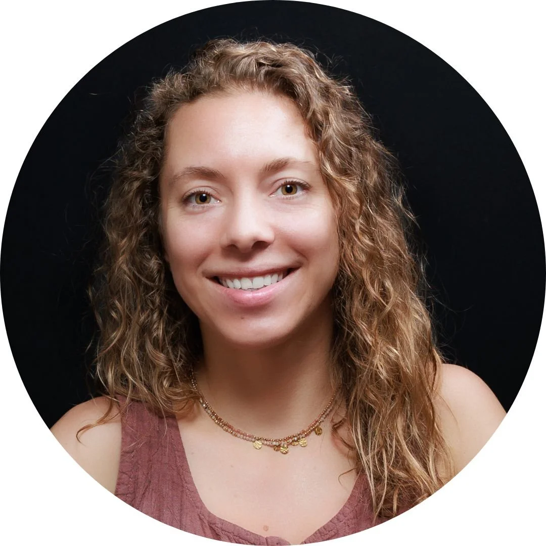 Close-up portrait of a young woman with curly light brown hair smiling against black background.