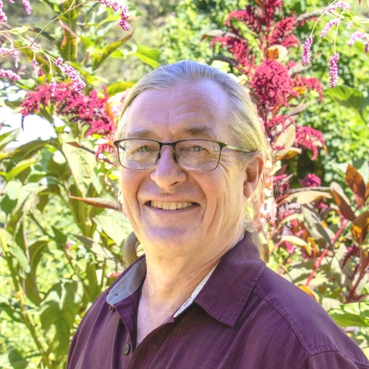 A middle-aged man with glasses, long hair tied back, wearing a light green shirt, smiling against a black background.