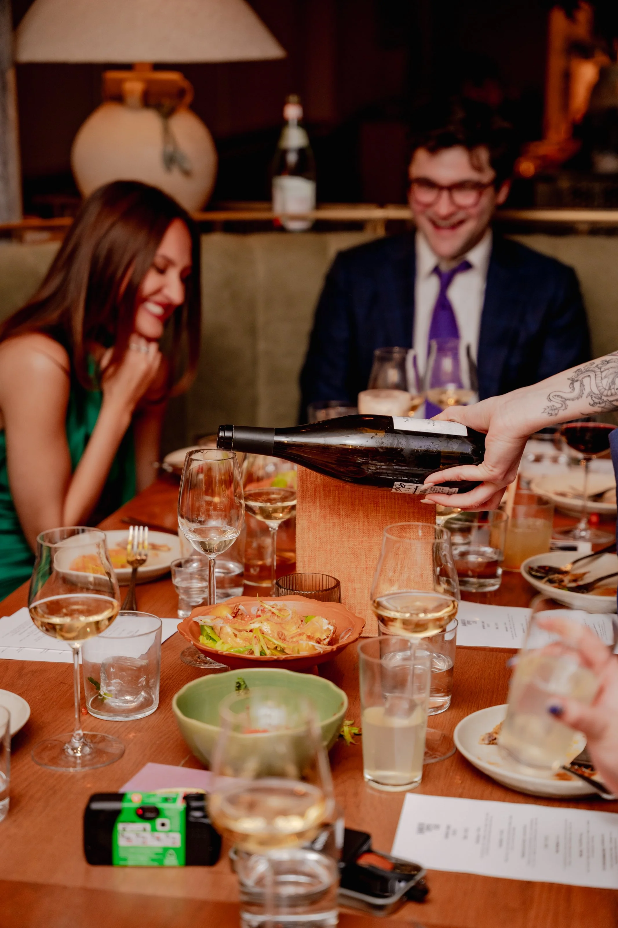People sitting at a dinner table being served wine in a restaurant. Bloom Vision Studio Emma Brawley