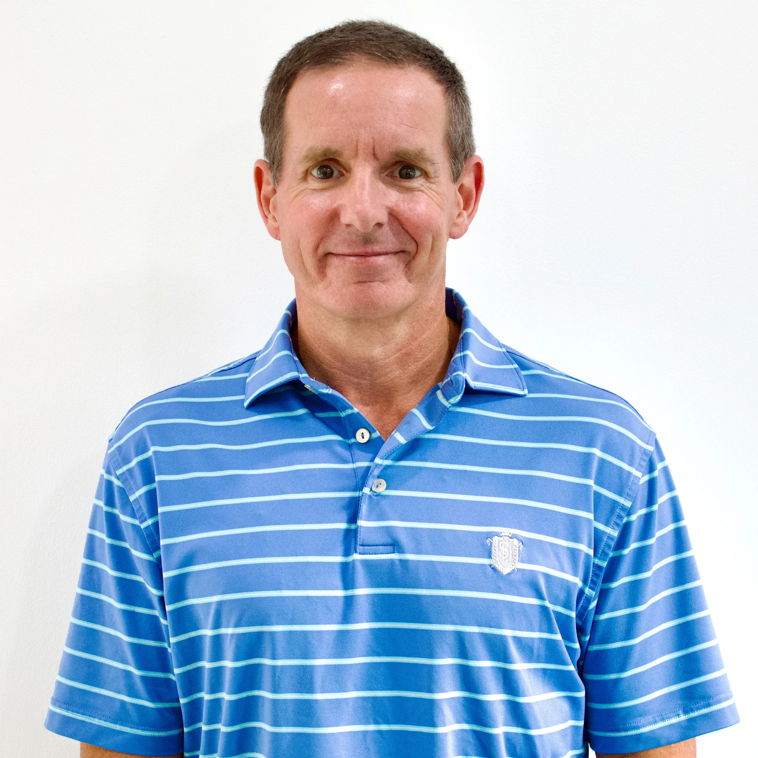 A middle-aged man with short brown hair, wearing a blue and white striped polo shirt, standing against a plain white background.