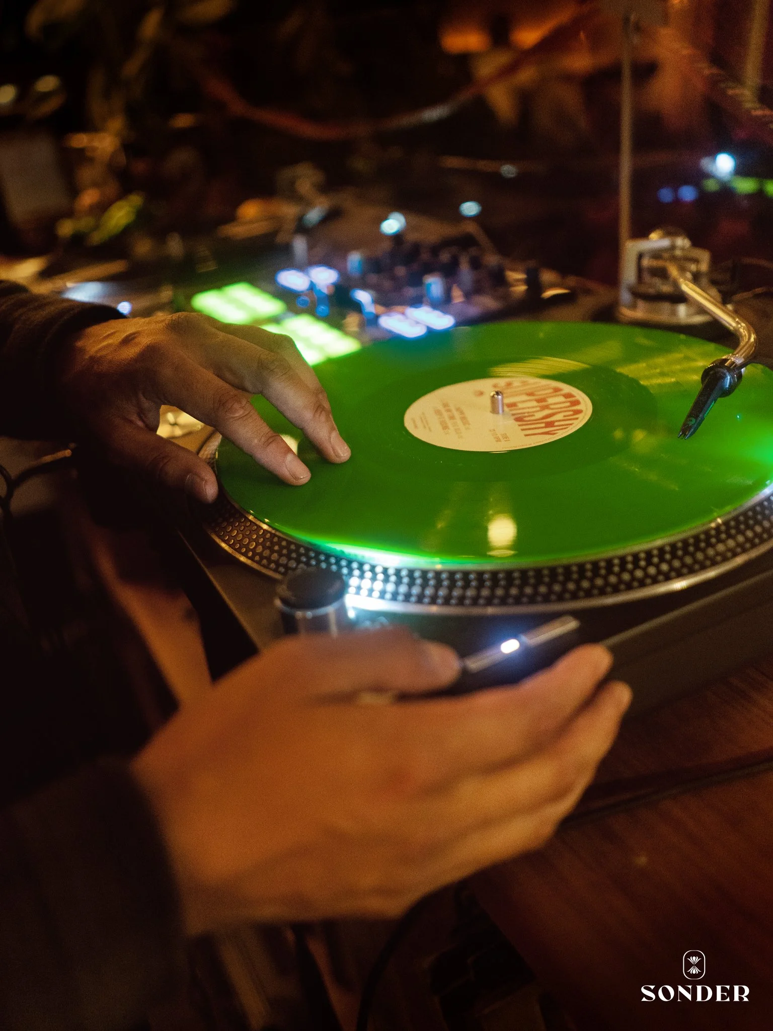 A DJ playing a green vinyl record on turntables in a dimly lit setting.