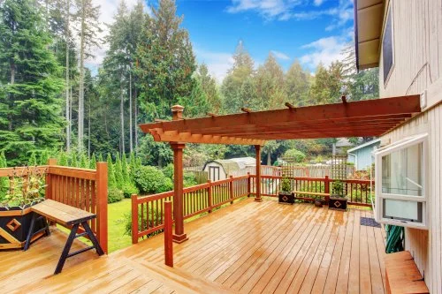 Wooden deck with pergola overlooking a lush garden with trees and a shed.