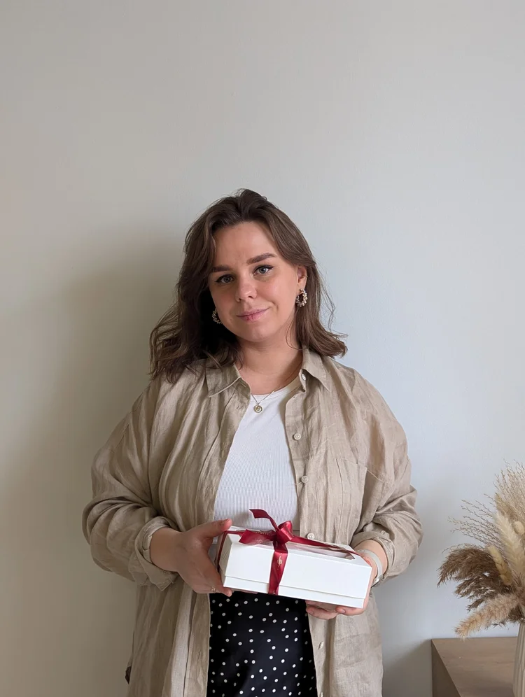 Julia, the baker behind JP Macarons, holding a white gift box tied with a red ribbon