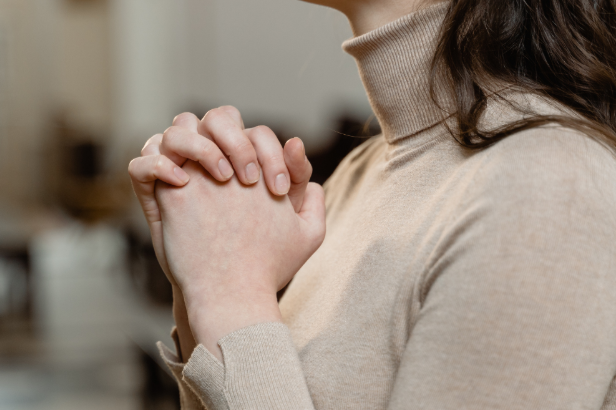 A person in a beige turtleneck clasps their hands together in prayer, conveying a sense of peace and reflection.