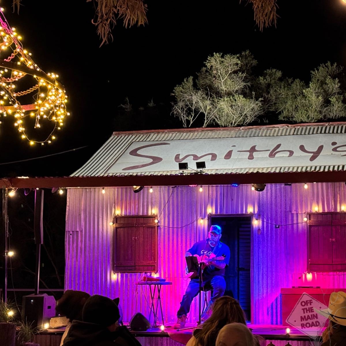 Musician performing on the corrugated iron stage at Smithy's outback show, Longreach, lit in pink and purple under fairy lights
